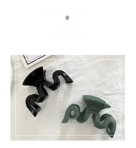 Detail of minimalist W-shaped large hair claw clips in black and dark green resin