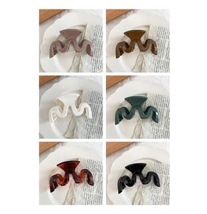 Detail view of large wave-shaped hair claws in six glossy colors on a ceramic plate