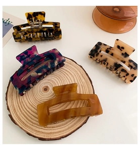 Detail showing square acetate claw clips in tortoiseshell and floral patterns on wood