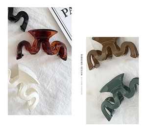 Detail showing five colors of wavy geometric hair claws on a textured linen background