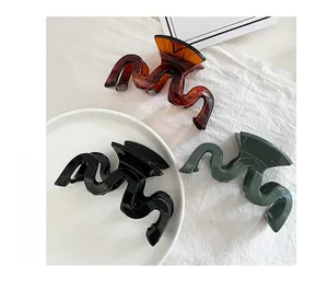 Close-up of wavy resin hair claws in black, amber, and green on white fabric background