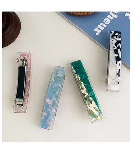 Detailed view of four acetate rectangular hair clips with marble patterns and metal springs