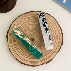 Elegant set of two marble and cow print acetate hair clips on a rustic wooden tray