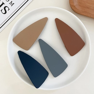 Matte geometric triangle hair clips in four Morandi colors set on a white ceramic plate