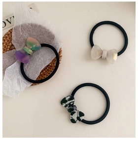 Close-up of three acetate bow hair ties in marble, pearlescent and cow print textures