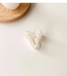 Detail shot of a small white pearlescent acetate hair claw clip with elegant wavy design