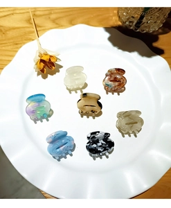 Close-up of small acetate hair claw clips in various colors displayed on a white plate