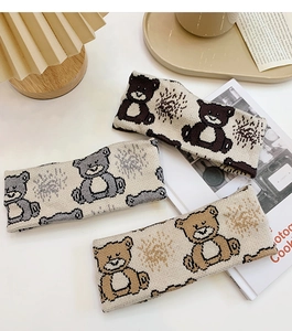 Three knit bear headbands in brown, grey, and khaki on a desk with a lamp