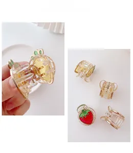 Primo piano di una mini molletta per capelli a fragola con molla dorata e dettagli smaltati