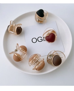 Mini heart-shaped hair clips in various colors arranged on a white ceramic plate