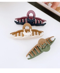 Close-up of three large matte plastic hair claws in contrasting color combinations on white