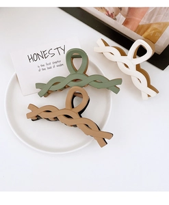 Close-up of three large matte resin hair claw clips in green, brown, and cream white colors
