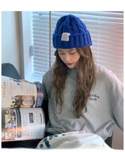 Close-up of royal blue chunky knit beanie with cable pattern and white logo patch