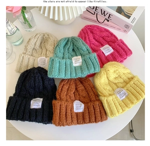 Flat lay of colorful chunky cable knit beanies with woven labels on a stylish white table