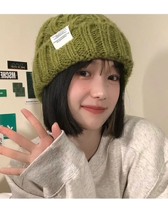 Detailed view of green chunky knit beanie with white woven label on a person