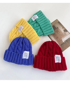 Detailed close-up of thick cable knit beanies in yellow, green, blue, and red with cloth labels