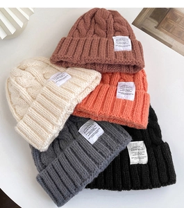 Flat lay of colorful thick cable knit beanies in coffee, cream, orange, grey, and black