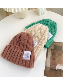 Close-up of thick cable knit beanies in brown, beige and green with woven fabric labels