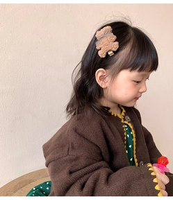 Détail d'une pince à cheveux ours en peluche marron avec nœud à carreaux sur un enfant