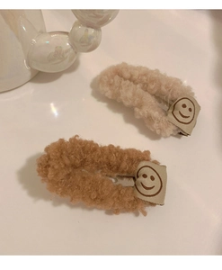Détail de barrettes en peluche beige et marron avec broderie de visage souriant