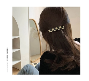 Dettaglio di un fermaglio per capelli vintage a scacchi neri e beige su una modella