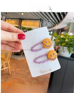 Close-up of two purple fabric hair clips with yellow smiley buttons on display card