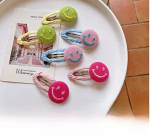 Close-up of six colorful embroidered smiley face fabric hair clips on a white ceramic tray