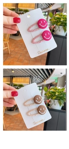 Detailed view of smiley face fabric hair clips in rose red and brown on display cards