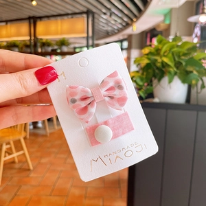 Close-up of pink floral bow hair clip and fabric button pin on display card