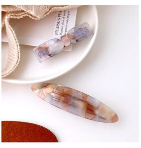 Detail of mermaid acetate bow and oval hair clips on a minimalist beige ceramic plate