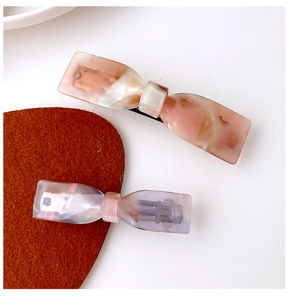 Detail view of acetate bow hair clips with marble texture in amber and lavender colors
