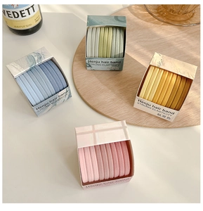 Close-up of pastel elastic hair ties in blue, green, yellow and pink boxes on a wooden tray