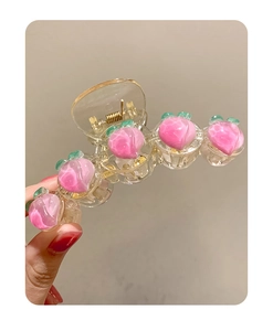 Détail d'une pince à cheveux avec motifs de pêches roses en acrylique tenue en main