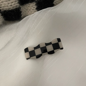 Barrette à cheveux à damier noir et blanc avec bord ondulé en acrylique sur tissu blanc