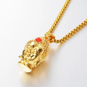 Macro detail of a golden Buddha head pendant with red gemstone and matching box chain