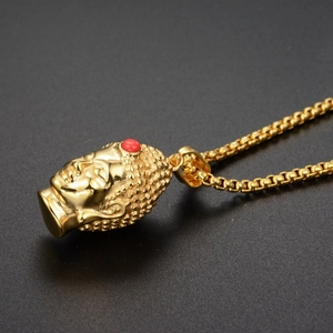 Detail view of a gold Buddha head pendant featuring a red bead on a box chain necklace