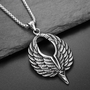 Collier avec pendentif tête d'aigle et ailes en acier argenté sur un fond en pierre sombre