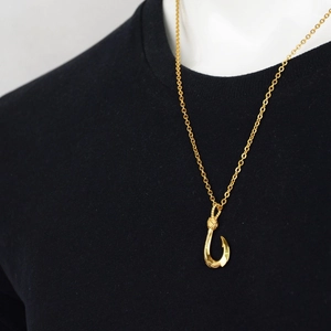 Polished golden Hawaiian fish hook necklace with engraved details on a black shirt