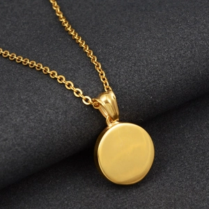 Close-up of a minimalist golden circular pendant necklace on textured grey fabric background