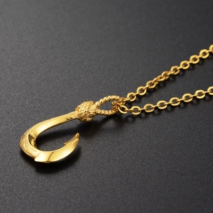 Close-up of golden fish hook pendant with detailed floral carvings and spiral top texture