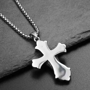 Gros plan du pendentif croix argenté avec chaîne vénitienne sur une surface en pierre