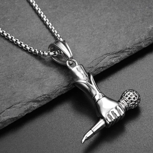 Detail of silver titanium hand holding microphone pendant on dark stone background