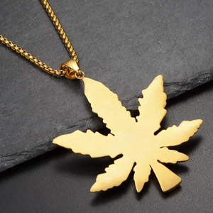 Macro shot of matte gold maple leaf pendant with metal brushed texture on beaded chain