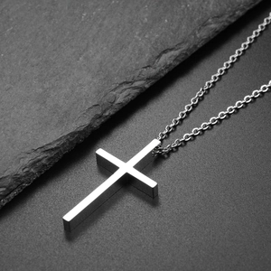 Vue macro du pendentif croix en acier poli sur un fond en pierre sombre texturé