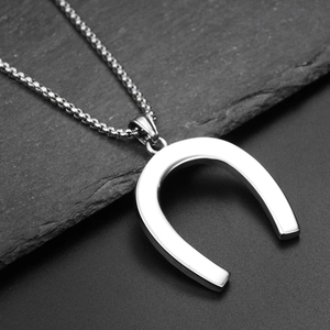 Détail macro d'un pendentif fer à cheval argenté avec chaîne box polie sur pierre sombre