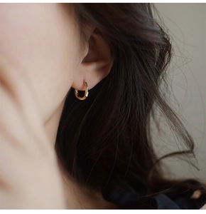 Primer plano de un pendiente de aro dorado Möbius con un elegante diseño de torsión