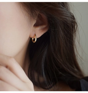 Primer plano de pendientes de aro dorados retorcidos minimalistas con reflejo metálico