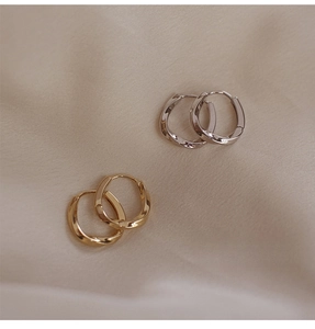Primer plano de pendientes de aro retorcidos en oro y plata sobre seda color beige