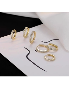 Dettaglio di tre orecchini huggie dorati con zirconi su seta e arte lineare minimal