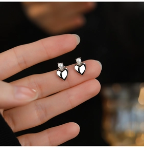 Close-up of S925 silver heart stud earrings with white pearl detail held by hand